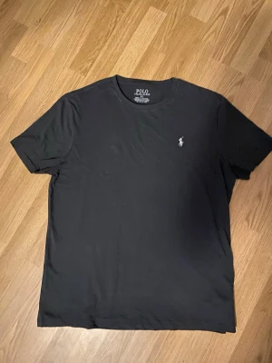 Svart t-shirt från Polo Ralph Lauren - Klassisk svart t-shirt från Polo Ralph Lauren med den ikoniska broderade loggan på bröstet. T-shirten har rund hals och korta ärmar, tillverkad i mjuk bomull för skön känsla. Perfekt basplagg med clean look.