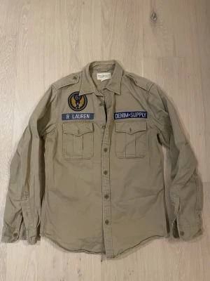 Beige overshirt från Ralph lauren  - Tjena!  Säljer nu denna super schyssta overshirten/skjortan från Ralph lauren. Skjortan är i storlek Medium och är i toppskick! Detta plagg är oerhört ovanlig då kollektionen denim & supply inte säljs längre! Vid fler frågor är det bara att höra av er.
