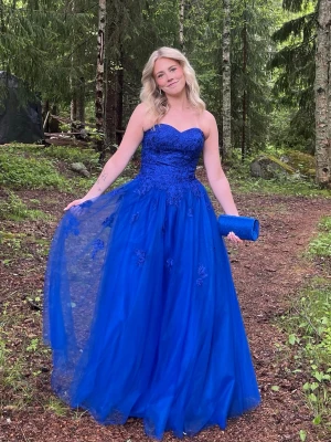 Blå balklänning med spetsdetaljer - Säljer en blå långklänning med hjärtformad överdel och spetsdetaljer. Klänningen har en kjol i tyll och är axelbandslös, perfekt för bal. Matchande blå clutch väska kan ingå om så önskas. Nypris 2000kr, använd endast en gång så säljer för 1800 men pris kan diskuteras