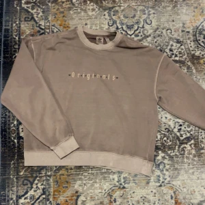Beige sweatshirt från Adidas Originals - Säljer en beige sweatshirt från Adidas Originals med trycket 'Originals' framtill. Tröjan har rund halsringning, långa ärmar och en relaxed passform. Perfekt för dig som gillar en enkel men snygg stil. Fint skick vintage 