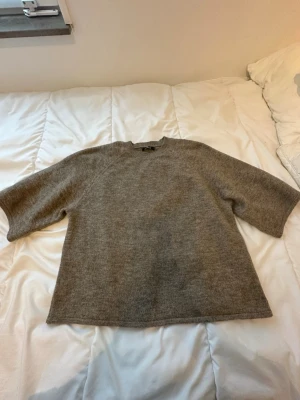 beige  stickad tröja med halvärm - Mysig grå stickad tröja med rund hals och halvärm. Tröjan har en enkel, clean look och är perfekt för lager på lager under höst och vinter. Materialet känns mjukt och värmande, och modellen är lite loose för en avslappnad vibe.