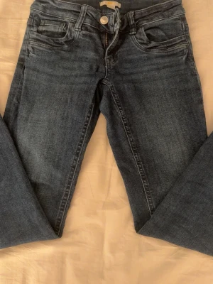 Mörkblå jeans från Gina Tricot - Snygga lågmidjade mörkblå jeans från Gina Tricot Young i klassisk femficksmodell. Jeansen har raka ben, normal passform och detaljer som dragkedja och knapp framtill. Perfekta till vardagslooken och funkar året runt.