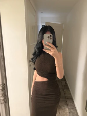 Brun långklänning med cut-out - Säljer en brun långklänning med snygg cut-out detalj i midjan. Klänningen är ärmlös och har en tight passform som framhäver figuren. Materialet är stretchigt och ger en bekväm känsla. Perfekt för dig som vill ha en trendig och stilren look. Använd en gång