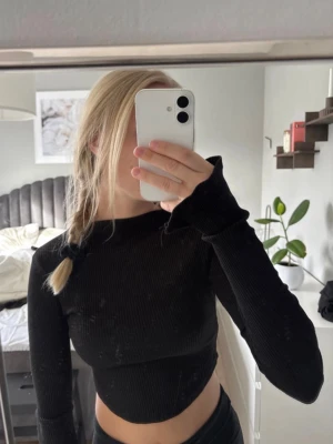 Svart ribbad croppad långärmad topp - Säljer en svart croppad topp med långa ärmar och ribbad struktur. Toppen har en tight passform och är tillverkad i mjukt stretchigt material. Ärmsluten har en liten slits för extra detalj. Perfekt att styla med höga jeans eller kjol.