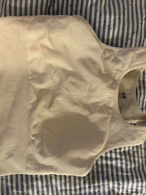 Vit ribbad linnetopp från H&M Sport - Säljer en vit ribbad linnetopp från H&M Sport i storlek M. Toppen har en sportig skärning med breda axelband och rund halsringning. Materialet är stretchigt och följsamt och har vaddering.