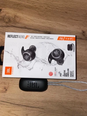 JBL Reflect Aero - JBL Reflect Aero trådlösa hörlurar med aktiv brusreducering, IP68-klassning för vattentäthet och dammtålighet. Perfekta för träning och samtal. Levereras med laddningsetui och extra öronproppar. Ser ut att vara i mycket gott skick utan synligt slitage.