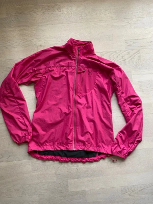Rosa vindjacka från Haglöfs - Säljer en snygg rosa vindjacka från Haglöfs med hel dragkedja framtill och hög krage. Jackan har en bröstficka med dragkedja, ficka i ryggslut. Elastisk över ryggen och tunt fodrad. Perfekt för utomhusaktiviteter.Storlek L