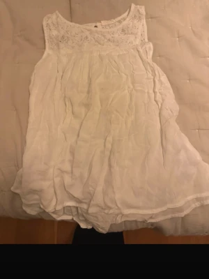 Vit ärmlös blus med spetsdetalj - Säljer en luftig vit blus med vacker spets upptill och rund halsringning. Blusen är ärmlös och har ett lätt, flowy tyg som ger en avslappnad känsla. Perfekt till sommaren och enkel att styla med jeans eller kjol.