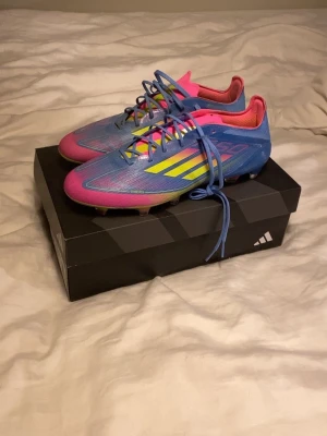 Adidas elite F50 färgglada fotbollsskor - Säljer ett par Adidas F50 fotbollsskor i en riktigt färgstark mix av blått, rosa och gult. Skorna har snörning, låg profil och är tillverkade i syntetmaterial för lätt vikt och speed. Ikoniska tre ränder på sidan och greppig dobbsula för bästa fäste på planen.helt oanvända 