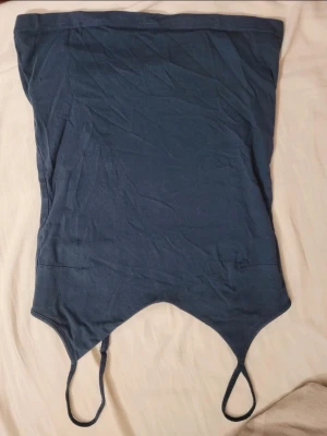 Mörkblå bandeau tubtopp - Säljer en mörkblå bandeau tubtopp med smala axelband och spetsig nederkant. Toppen är enkel och stilren, perfekt för sommardagar eller festivaler. Materialet känns mjukt och stretchigt, vilket gör den bekväm att bära.