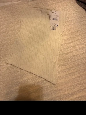Offwhite ribbad tubtopp från NA-KD - Säljer en offwhite ribbad tubtopp från NA-KD i storlek XS. Toppen har en strukturerad yta med vågiga detaljer och en liten slits på sidan för extra stil. Perfekt att matcha med höga jeans eller kjol för en clean look.
