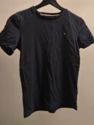 Mörkblå t-shirt från Tommy Hilfiger - Snygg mörkblå t-shirt från Tommy Hilfiger med klassisk passform och liten logga på bröstet. Tillverkad i mjuk bomull och har rund hals samt korta ärmar. Perfekt till jeans eller shorts för en clean look.
