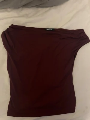 Vinröd oneshoulder topp Gina Tricot - Säljer en vinröd oneshoulder topp från Gina Tricot. Toppen har en tight passform och ärmlös design med asymmetrisk axel. Materialet är mjukt och stretchigt, perfekt för att skapa en snygg siluett. Enkel och stilren utan mönster eller detaljer.