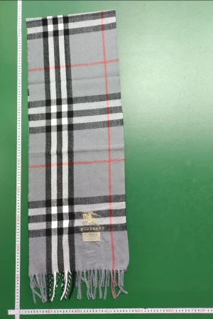 Grå rutig bur halsduk - Snygg halsduk i klassiskt rutigt mönster med grå, svart, vit och röd färg. Halsduken har fransar i ändarna och ett broderat -emblem i guld. Perfekt accessoar för att lyfta din outfit.