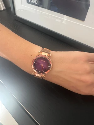 Lila Ulzzang klocka med roséguld meshband - Snygg klocka från Ulzzang med lila urtavla och roséguldfärgat mesharmband. Urtavlan har en facettslipad kant och små kristalldetaljer vid varje timmarkering. Klockan har minimalistisk design och ett elegant metallspänne. Perfekt accessoar för att lyfta din stil.