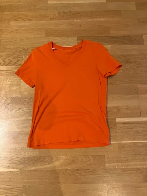 Orange t-shirt med v-ringning - Snygg orange t-shirt med v-ringad hals och korta ärmar. Enkel och stilren design som passar perfekt till jeans eller shorts. Tillverkad i mjuk bomull för skön komfort hela dagen. Perfekt för dig som gillar färgstarka plagg och vill sticka ut lite extra.