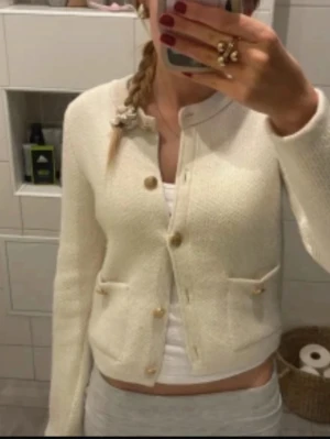 Krämvit kofta med knappar - Superfin krämvit kofta från H&M med rund halsringning och snygga guldiga knappar framtill. Koftan har fyra dekorativa fickor och är stickad i ett mjukt material. Perfekt att slänga över en topp för en clean och chic look. OBS första bilden är lånad och det är den på bild 2 som jag säljer 