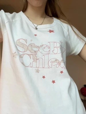  Chloé t-shirt  - Supersöt vit t-shirt från Chloé, See By Chloé med röd text och stjärnor på framsidan. Modellen är klassisk med rund hals och korta ärmar. Materialet är mjuk bomull som känns skönt mot huden. Perfekt för dig som gillar coola designer och vill sticka ut lite extra. Pris kan diskuteras! Tveka inte vid frågor💕💕