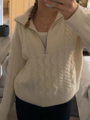 Vit stickad tröja med half zip - Mysig vit stickad tröja med kabelstickat mönster och half zip-dragkedja vid kragen. Tröjan har långärmad design och en lite loose passform, perfekt för kyliga dagar. Snygg och enkel att matcha till olika outfits.