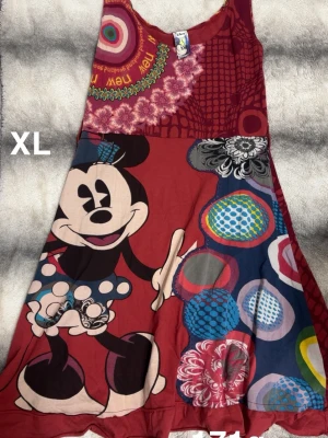 Desigual x Disney klänning XL - Färgstark kortklänning från Desigual i samarbete med Disney, med stor Minnie Mouse-tryck framtill och broderad guldig Musse Pigg-detalj. Klänningen har blandade mönster i rött, blått och beige samt blommiga och prickiga inslag. Tillverkad i mjuk bomull, ärmlös och med rund hals.🌸 Fint använt skick. Fick i present men passar inte mig längre. Saknar skärp. Storlek XL