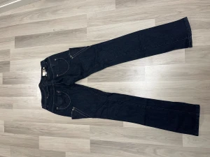 Mörkblå jeansbyxor från R.Marks - Snygga mörkblå jeansbyxor från R.Marks med coola detaljer som dekorativa sömmar, nitar och extra fickor framtill. Klassisk femficksmodell med raka ben och låg midja. Perfekta för dig som gillar en unik och trendig jeansstil.