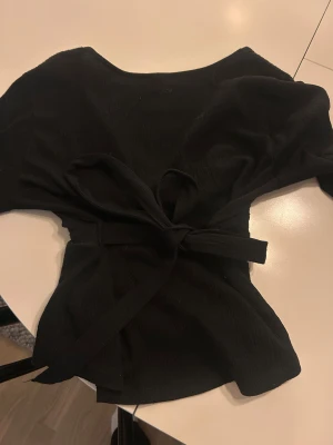 Svart blus med knytning  - Svart blus med knytning som man kan knyta både fram och baktill ifrån Gina i storlek xs. Bara använd några få gånger och har inte några skador eller defekter!