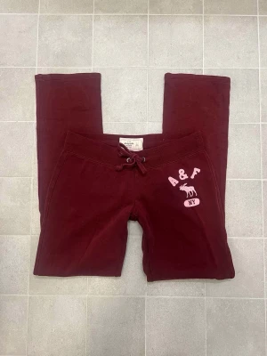 Amercrombie byxor - Snygga vinröda lågmidjade mjukisbyxor från Abercrombie & Fitch med rosa broderad logga och älg på vänster höft. Storlek S.