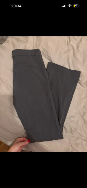 Grå kostymbyxor från 157 XS - Snygga grå kostymbyxor från 157 i storlek XS. Byxorna har raka ben, hällor för bälte och en klassisk look. Perfekta för dig som gillar stilrena och enkla plagg. Materialet känns mjukt och bekvämt mot huden.