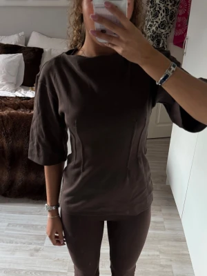 Brun topp med trekvartsärm - Säljer en mörkbrun topp med trekvartsärm och rund hals. Tröjan går in lite i midjan sen utåt mot höfterna, använd 1 gång. Sitter som en s / xs