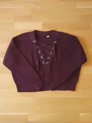 Stickad tröja - Vinröd stickad tröja från Gina Tricot med snygg snörning framtill. Tröjan är croppad, har långa ärmar och är ribbad i materialet. Perfekt för dig som vill ha en trendig och mysig look i höst och vinter.