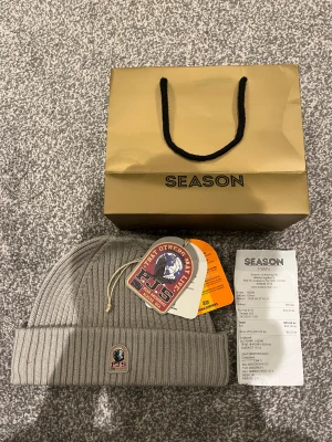 Grå ribbad mössa från Parajumpers - Sprillans ny snygg grå ribbstickad mössa från Parajumpers med broderad PJS-logga framtill och röd etikett på insidan. Mössan är i one size och har en klassisk uppvikt kant. Perfekt för kalla dagar och riktigt stilren. Köpt på Season på Asecs. Nypris: 800kr, mitt pris: 699kr. 