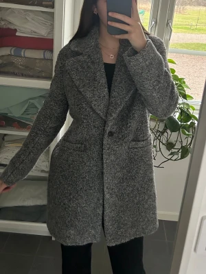 Grå fluffig kappa  - Snygg grå kappa med bred krage och en knapp framtill. Jackan har en mjuk, lite fluffig struktur och två fickor på sidorna. Finns även innerfoder i jackan så man håller sig varm även på vintern
