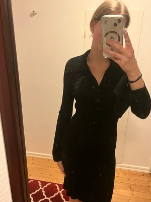 Svart ribbad klänning från Gina Tricot - Svart, ribbad klänning med lång ärm och krage från Gina Tricot. Klänningen har knappar framtill och en figurnära passform som ger en snygg siluett. Perfekt för dig som gillar stilrena och enkla plagg med en twist.