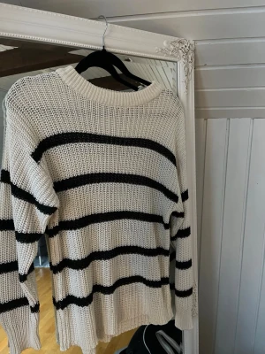 Vit och svart randig stickad tröja - Säljer en vit stickad tröja med svarta horisontella ränder. Tröjan har rund hals, långärmade ärmar och en loose passform. Perfekt för dig som gillar en chill och avslappnad stil. Materialet är grovstickat och mjukt.