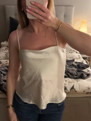 Vitt satin linne - Vitt satin linne från Gina Tricot i storlek M. Vill man att det ska sitta lite lösare (som mig) passar det bra på en XS/S. De är aldrig använt därför i nyskick. Passar fint nu till jul och nyår med t.ex en kavaj. Banden kan jag justera så det passar bra. Hör gärna av dig vid frågor🤍