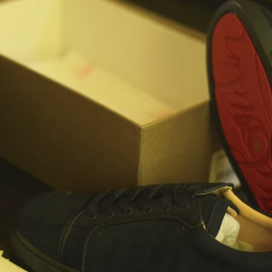 Mörkblå sneakers från Christian Louboutin - Exklusiva mörkblå sneakers från Christian Louboutin med ikonisk röd sula och snygg snörning. Skorna har en stilren design med rund tå och platt sula, tillverkade i skinn för en lyxig känsla. Perfekt för dig som vill sticka ut med ett statement-märke.