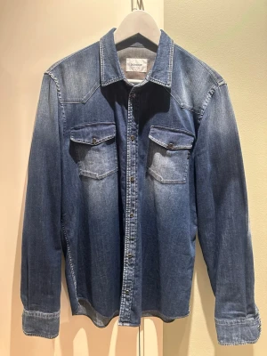 Jeansskjorta från Dondup - Snygg jeansskjorta från Dondup i klassisk blå denim. Skjortan är i nyskick, endast använd ett par gånger. Inköpt på Ströms för 2700 kr