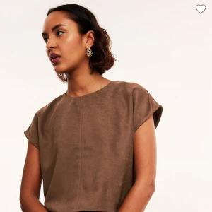 Brun mockaliknande topp från Kappahl - Säljer en brun mockaliknande topp från Kappahl i storlek XS. Toppen har rund hals, korta ärmar och en rak, croppad passform. Materialet är mjukt och har en snygg matt yta. Stängs med en liten knapp i nacken. Perfekt att styla med jeans eller kjol.