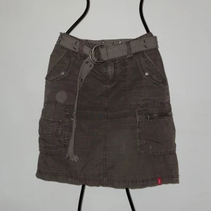 Cargokjol med bälte från edc by esprit - Säljer en cargo midikjol från edc by esprit med tillhörande bälte. Kjolen har flera fickor med dragkedja och knappar, samt ett grovt tygbälte med metallspänne. Perfekt för en avslappnad och cool stil. Bältet har en liten defekt, se bild 4.
