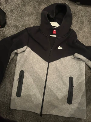 Nike tech  - Grå-svart Nike tech Storelk M/L fin och dragkedjan och en liten fläck finns inget man märker 