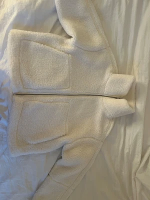 Vit teddyjacka  - Mysig vit teddyjacka från ONLY i storlek XL. Jackan har hög krage, två stora fickor framtill och dragkedja. Perfekt för höst och vinter.