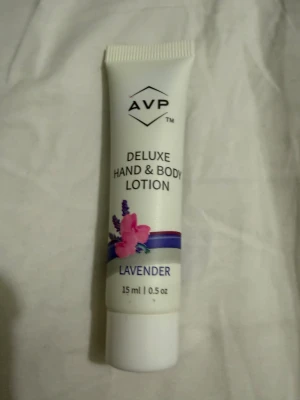 AVP Deluxe Hand & Body Lotion - En liten tub med AVP Deluxe Hand & Body Lotion, doft av lavendel. Tuben är vit med lila och rosa detaljer och har en bild på en lavendelblomma. Innehåller 15 ml, perfekt att ha med i väskan för mjuka händer. Helt ny!!