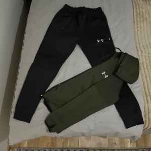 Tracksuit från Under Armour - Tracksuit från Under Armour med vit logga på benet och snörning i midjan. Byxorna har en slim passform och är perfekta för träning eller chill. Materialet är mjukt och stretchigt, med praktiska fickor och ribbade muddar vid bensluten.