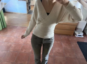 Beige omlott stickad tröja - Supersnygg beige stickad tröja med omlott-design och v-ringad hals. Tröjan har ribbade detaljer och långa ärmar, sitter tajt i midjan och ger en riktigt fräsch siluett. Perfekt för dig som gillar trendiga och bekväma plagg med lite extra stil. Toppen är köpt på vinted, aldrig använd av mig då den inte kom till användning❣️