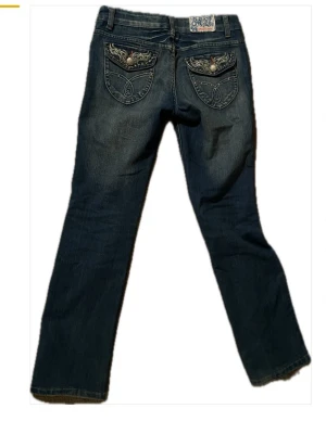 Blå lowaisted Onado jeans med broderade fickor - Snygga blå jeans från Onado med broderade detaljer och knappar på bakfickorna. Jeansen har normal passform, raka ben och klassisk femficksdesign. Materialet är jeans i bomull och de har coola slitningar framtill för en trendig look. Skulle säga att tvätten är lite ljusare än vad de visas i bilden! Men sista bilden visar rätt bra vilken färg de är! 