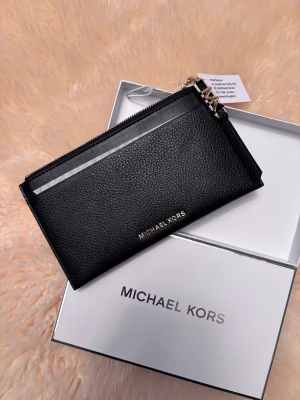 Michael Kors - Akta Michael Kors plånbok i svart läder - helt ny! Mått: djup 10,5 cm, bredd 0,5 cm, total längd 19 cm