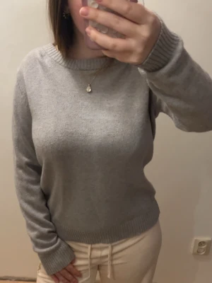 Ljusgrå stickad tröja - En enkel och stilren ljusgrå stickad tröja med rund halsringning och ribbade muddar vid ärmslut och nederkant. Tröjan har en mjuk och skön ullmix som passar perfekt till kyligare dagar. Klassisk passform och tidlös design.