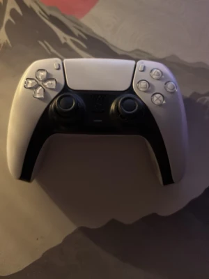Vit Sony DualSense PS5 handkontroll - Säljer en vit Sony DualSense handkontroll till PlayStation 5. Kontrollern har svart detaljdesign, två analoga spakar, touchpad och klassiska PlayStation-knappar. Ergonomisk form och tillverkad i plast. Perfekt för gaming på PS5.