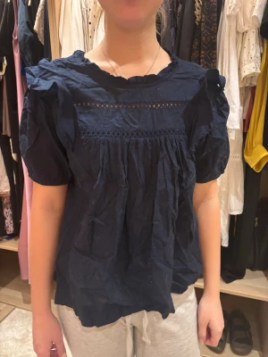 Mörkblå blus med puffärm Gina Tricot - Snygg mörkblå blus från Gina Tricot med puffärmar och dekorativa spetsdetaljer vid bröstet. Blusen har rund halsringning och är gjord i ett lätt, vävt material som ger en luftig känsla. Perfekt att styla med jeans eller kjol för en trendig look.