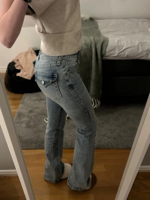 Ljusblå bootcut jeans True Religion - Säljer ett par ljusblå jeans från True Religion med bootcut passform och snygga detaljer på bakfickorna. Klassisk femficksmodell och mid midja. Perfekta för dig som gillar en avslappnad men trendig look. Använt dem väldigt få gånger 💘